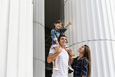 Family of three standing near pillars, young child on man's shoulders