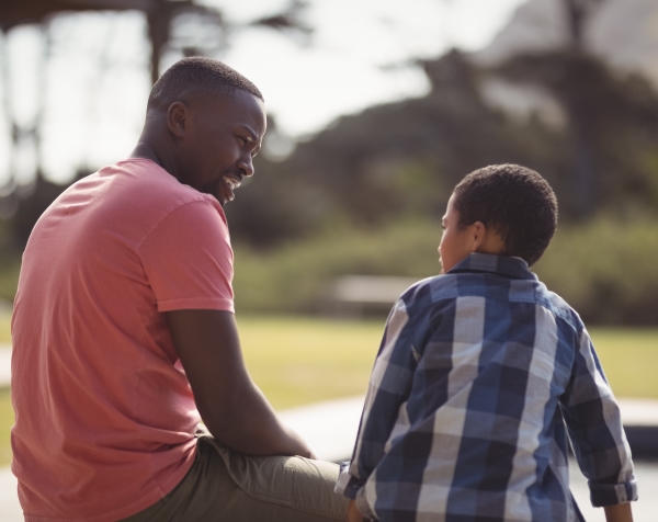 A father and son sitting on a bench having a conversation facing each other