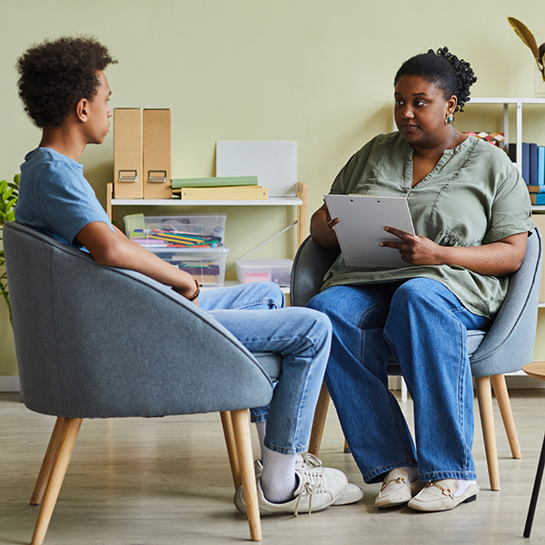 A young boy sitting in an office talking to a young black social worker